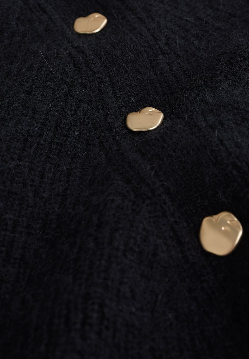 Zwart, gestructureerd breiwerk met drie gouden, hartvormige knopen die gelijkmatig langs het midden zijn geplaatst. Zacht en fuzzy materiaal.