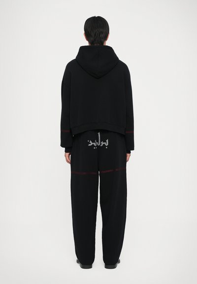 Set di felpa con cappuccio e pantaloni neri realizzato in tessuto morbido, con un design corto, dettagli di cuciture rosse e testo stampato sulla schiena.
