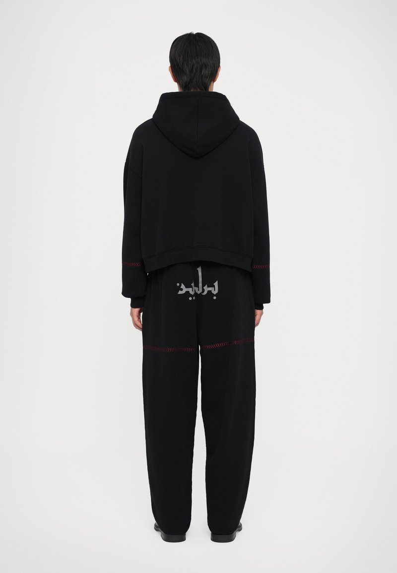 Sæt bestående af sort hættetrøje og bukser lavet af blødt stof, med et cropped design, røde syninger og trykt tekst på ryggen.
