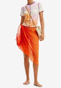 Multibarevný tie-dye top s krátkými rukávy, v odstínech oranžové a fialové. Průhledná oranžová zavinovací sukně s texturovaným vzorem. Woven kabelka jako doplněk.