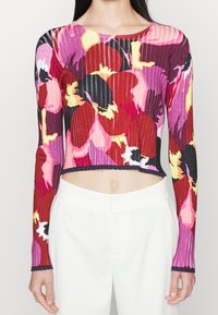 Hedvábný pletený crop top v živých květinových vzorech v odstínech červené, růžové a žluté. Má dlouhé rukávy a kontrastní lem.