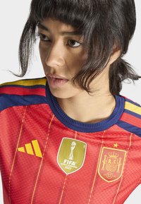 Red jersey with blue accents, featuring yellow stripes. Displays FIFA Women’s World Cup logo and Spanish national emblem on the front.