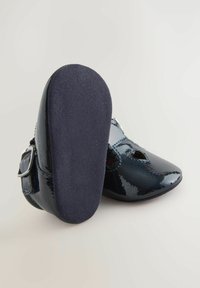 Granatowe buty z lakierowanej skóry patentowej z okrągłym noskiem, paskiem z klamrą, kwiatowymi wycięciami oraz teksturowaną podeszwą zapewniającą przyczepność.