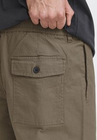 Shorts cargo vert olive en tissu texturé, avec une poche arrière munie d'un bouton noir et une taille élastique.