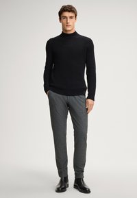Schwarzer gerippter Rollkragenpullover, kombiniert mit grauen strukturierten Hosen und schwarzen Stiefeletten, bestehend aus einem taillierten Design und langen Ärmeln.
