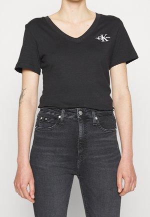 Czarny bawełniany T-shirt z dekoltem w serek i krótkimi rękawami, z małym białym logo na lewej piersi. Połączony z ciemnymi dżinsami.