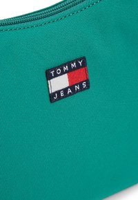 Πράσινη υφασμάτινη θήκη με ορθογώνιο ταμπελάκι λογότυπου Tommy Jeans σε αποχρώσεις του ναυτικού μπλε, κόκκινου και λευκού. Υφή με φερμουάρ κλεισίματος.