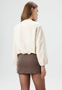 Crèmekleurige blouse met ballonmouwen, elastische zoom, gecombineerd met een bruine minirok. Gladde stof en een aansluitend ontwerp.