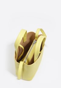 Mała żółta skórzana torebka z dwoma uchwytami i centralną przegródką na suwak, pokazana otwarta na białym tle.