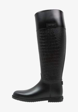 Černé gumové holínky do kolen s texturovaným vzorem připomínajícím ještěrku na svrchní části, hladkým povrchem na spodní části a detailem loga.