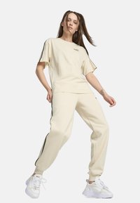 Camiseta oversized crema de manga corta, combinada con pantalones de chándal a juego que presentan tiras laterales negras. Zapatillas blancas completan el look.