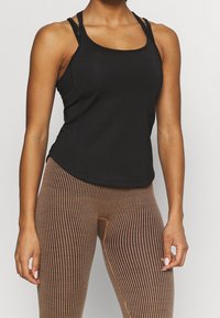 Top deportivo negro sin mangas con tirantes finos, combinado con leggings marrones a rayas con cintura alta y tejido texturizado.