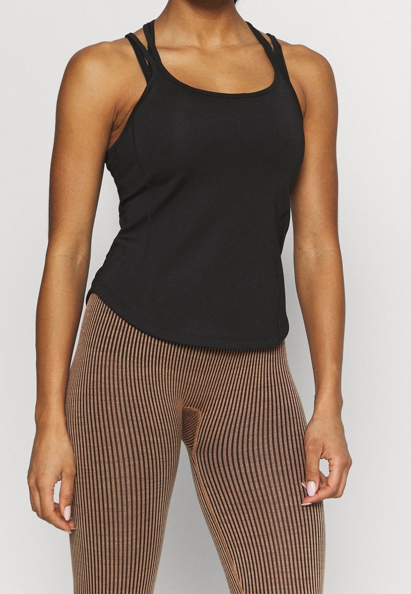 Top deportivo negro sin mangas con tirantes finos, combinado con leggings marrones a rayas con cintura alta y tejido texturizado.