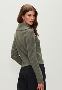 Grüner, gerippter Pullover mit umgeschlagenem Kragen und langen Ärmeln. Eng anliegendes Design, strukturierter Stoff und ein verkürzter Schnitt.
