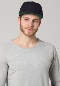 Gorra negra con visera verde, tejido texturizado, diseño de seis paneles. Sudadera gris con cuello redondo y mangas raglán, tejido liso.