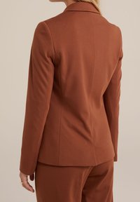 Brun skräddarsydd kavaj med långa ärmar, strukturerad tyg, notchad krage och figursydd silhuett, som visar ett slätt baksömmar.