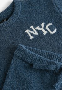 Blauwe wollen trui met geribde halslijn en manchetten, met 'NYC' geborduurd in crème. Textuur met een zachte afwerking en een relaxed fit.