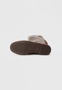 Sola de sapato em borracha castanha e texturizada, com material superior liso em bege claro e uma ligeira curvatura no calcanhar.