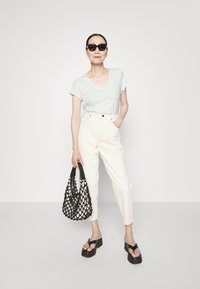 Gaiši zils V-veida t-krekls, baltas augstām jostasvietām bikses, melnas platformas sandales un melna austs totē soma ar atvērtu acu dizainu.