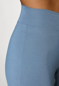 Høytlivsleggings i myk blått stoff. Glatt tekstur med tettsittende passform. Ingen synlige sømmer eller mønstre, som fremhever et minimalistisk design.