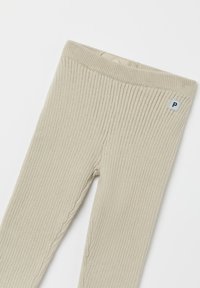Ribbed beiget legginsit, joissa on pehmeä rakenne ja joustava vyötärö. Lantiolla on pieni sininen tagi, jossa on valkoinen kirjain "P".