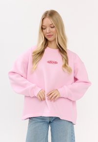 Felpa rosa con scollatura tonda, maniche lunghe e polsini a costine. Presenta un ricamo frontale in rosso. Tessuto morbido.