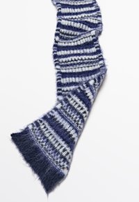 Sciarpa a righe con una texture morbida e pelosa; i colori includono blu navy, grigio chiaro e bianco; presenta larghezze di strisce variabili e estremità frangiate.