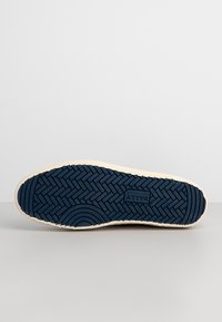 Semelle d'une chaussure décontractée avec une semelle en caoutchouc bleu marine présentant un motif en chevrons et des courbes concentriques, marquée « Bally Switzerland » au centre.