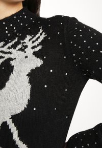 Svart stickad tröja med ett ren-design i grått, prydd med små klara rhinestones utspridda över tyget.