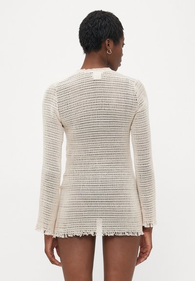 Neulepeitehuppu off-white-värissä, jossa on löysä kudontatyyli, pitkät hihat ja spagettihelma. Yksinkertainen muotoilu suoralinjaisella leikkauksella.