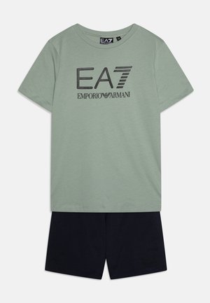 T-shirt in cotone verde chiaro con logo EA7 Emporio Armani nero, abbinato a pantaloni corti in cotone blu navy con un logo discreto sull'orlo.