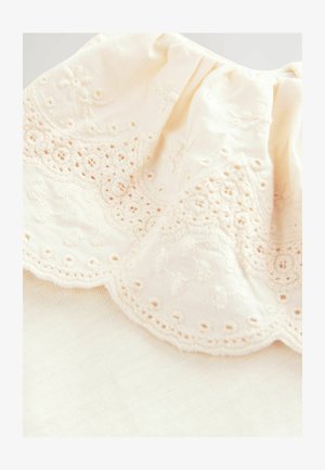 Kreemi värvi kangas, millel on keerukad pitsid kaeluses, sisaldades lillemustreid ja lainesid. Pehme tekstuur.