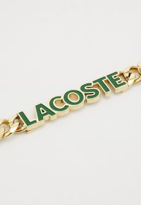 Brățară din aur cu litere verzi ridicate "LACOSTE", având verigi lustruite și netede, creând un design îndrăzneț și vibrant.