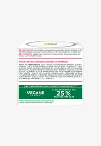 Biały kwadratowy pakunek z zielonymi akcentami, z wyraźnym tekstem w wielu językach. Zawiera listę składników, informacje o recyklingu oraz instrukcje użytkowania.