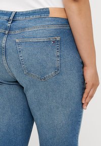 Μπλε τζιν παντελόνι με κοντινή λήψη που δείχνει μια πίσω τσέπη και δερμάτινη ετικέτα. Έχει ελαφριά φθορά και δομημένη εφαρμογή.