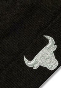 Schwarze Strickmütze mit strukturierter Oberfläche und einem auffälligen, silbernen, gestickten Stierlogo auf der Vorderseite.