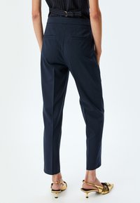 Pantaloni sartoriali blu navy con vita media, due tasche posteriori e una linea dritta elegante. Abbinati a décolleté oro con cinturino.