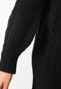 Maglione nero lavorato a maglia con un design a trecce testurizzato, polsini a costine e una forma rilassata, realizzato in un filato morbido e caldo.