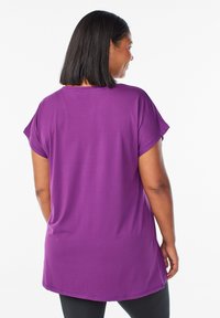 Lilla kortærmet tunika med rund udringning og længere baghem. Lavet af et blødt, let stof med en glat overflade.