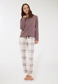 Długi rękaw w kolorze mauve z falbaniastym wykończeniem, w połączeniu z białymi spodniami w kratkę w pastelowych odcieniach. Miękka tkanina o luźnym kroju.