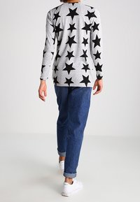 Maglietta grigia a maniche lunghe decorata con motivi a stella nera, abbinata a jeans in denim blu arrotolati e sneakers bianche, vista da dietro.