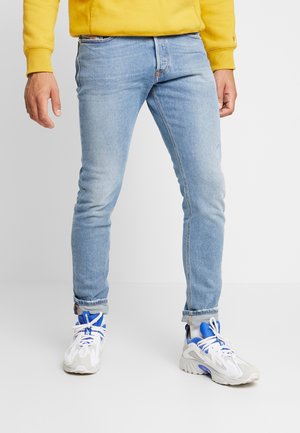 Vaqueros de mezclilla azul claro con un ajuste slim, que presentan un dobladillo enrollado; combinados con zapatillas deportivas blancas y azules. Textura suave, diseño clásico.