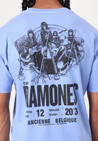 Light blue cotton t-shirt featuring a black graphic print of The Ramones band members and concert details at the back. Short sleeves, casual fit.