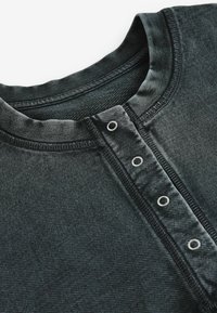 Gros plan sur une chemise texturée gris foncé montrant un col rond et une patte de boutonnage avec quatre boutons-pression argentés.