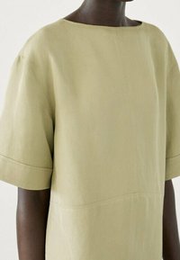 Haut vert pâle à manches courtes avec encolure bateau, fabriqué en tissu lisse. Présente un design minimaliste et des coutures structurées.