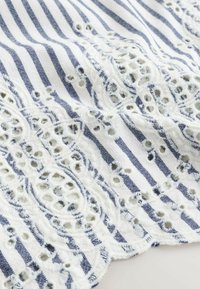 Hvid og blåstribet stof med broderede hulmønstrede blonder og bølgete kanter.