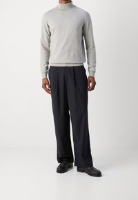 Grå strikket rullekravesweater, kombineret med marineblå bukser med fine striber. Sorte loafers fuldender outfittet. Markante lodrette striber.