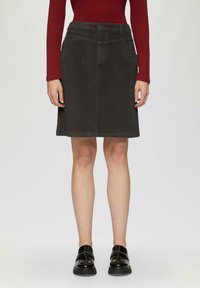 Jupe en velours côtelé grise avec une coupe droite, des poches latérales et des passants de ceinture. Associée à un haut ajusté à manches longues rouge et des chaussures noires.
