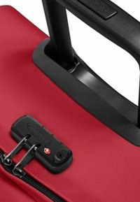Red suitcase with a textured fabric surface, a black retractable handle, and a TSA-approved zipper lock for security.