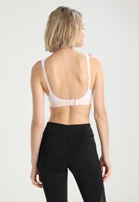 Hvit bh med justerbare stropper og krok-lukking bak, kombinert med høy midje svarte leggings. Glatt tekstur og minimalistisk design.